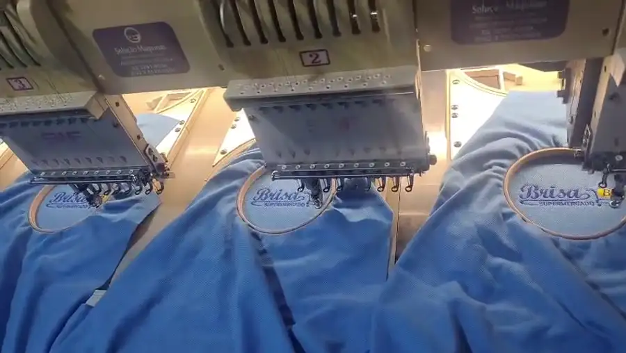 Máquina de bordado computadorizado aplicando logomarca em uniforme na América Uniformes