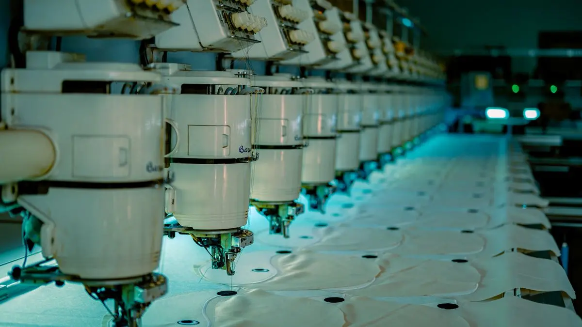 Linha de máquinas de costura industriais em fábrica de confecção produzindo uniformes