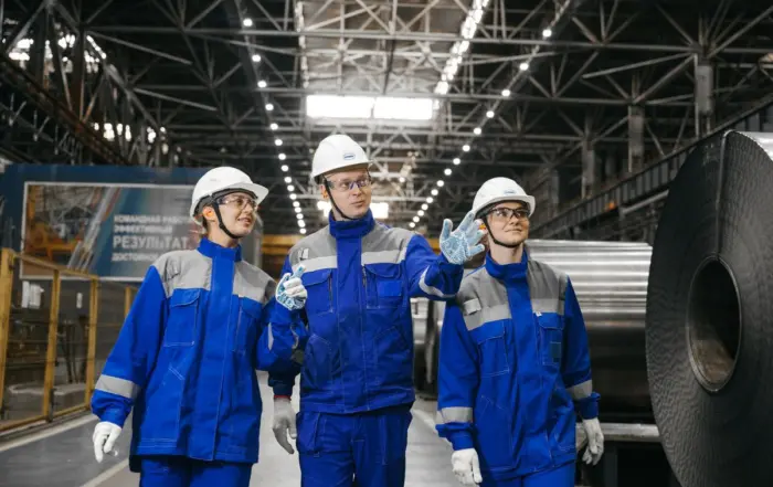 Equipe de trabalhadores com uniforme profissional azul e equipamentos de proteção (capacete e luvas) em fábrica industrial