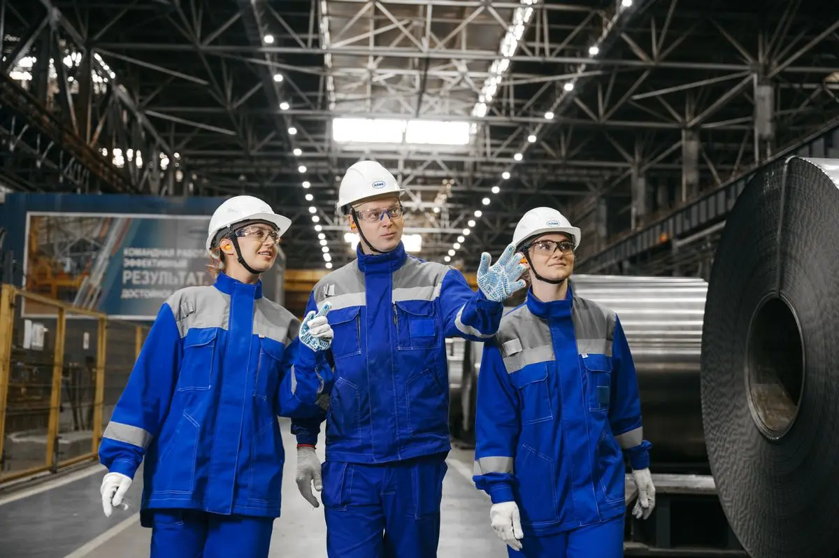 Equipe de trabalhadores com uniforme profissional azul e equipamentos de proteção (capacete e luvas) em fábrica industrial